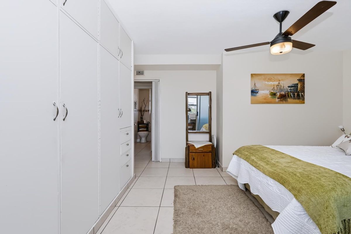 A well-maintained bedroom featuring built-in cupboards, tiled flooring, a ceiling fan, and direct access to an en-suite bathroom.