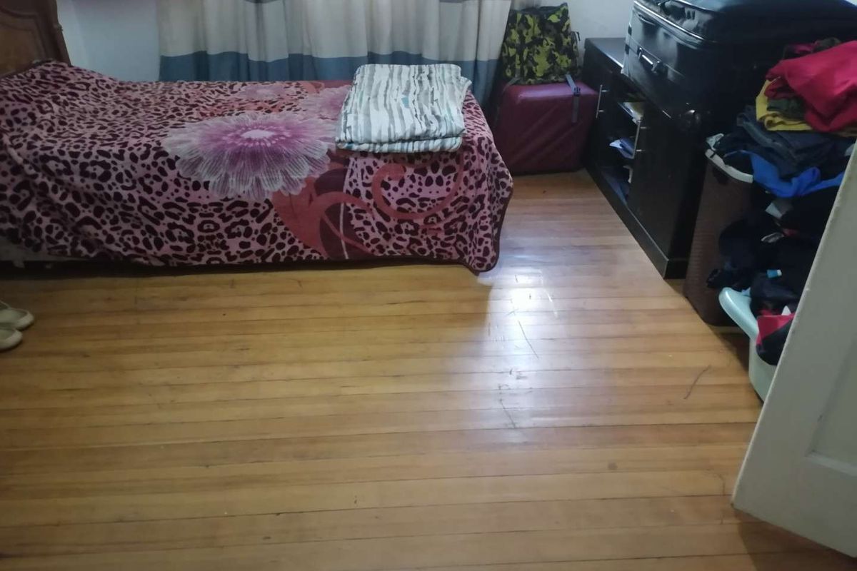 A bedroom featuring polished timber flooring and a window with curtains.