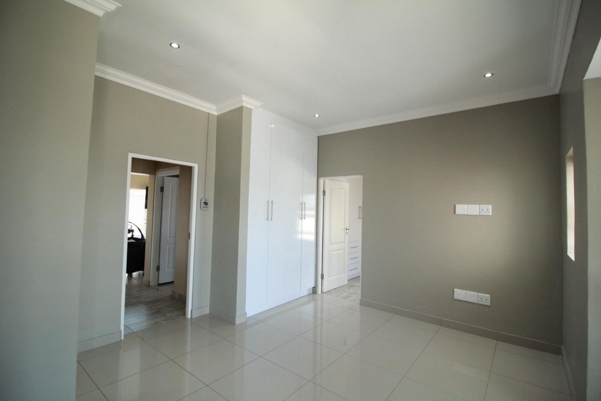 A bright, empty bedroom featuring neutral walls, tiled flooring, recessed downlights, and modern white built-in cupboards.