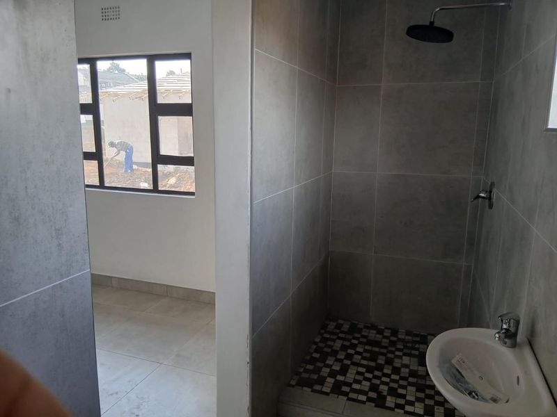 A modern bathroom featuring grey wall tiles, a walk-in shower with a rain shower head, and a wall-mounted basin.