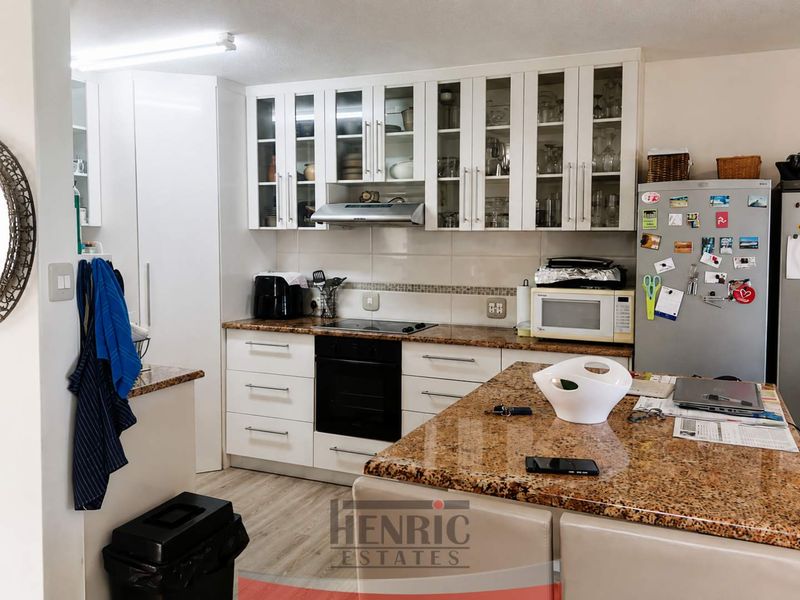 A functional kitchen featuring granite countertops, white cabinetry with glass-fronted upper units, a built-in oven, and an electric hob.