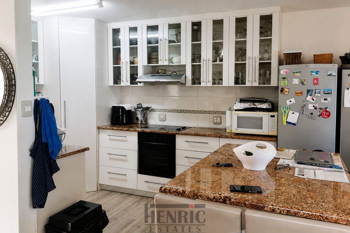 A functional kitchen featuring granite countertops, white cabinetry with glass-fronted upper units, a built-in oven, and an electric hob.