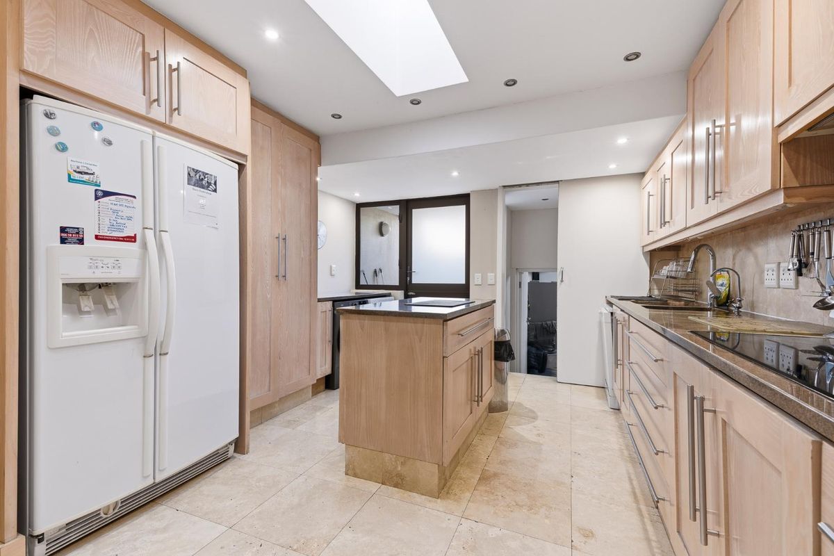 A functional kitchen featuring light wood cabinetry, stone countertops, a central island, integrated lighting, and a skylight, providing a bright and practical workspace.