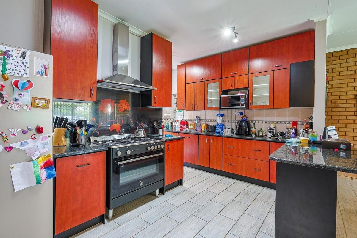 A functional kitchen featuring wood-toned cabinetry, granite countertops, a gas stove with an extractor fan, and tiled flooring.