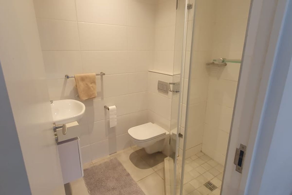 A compact, modern bathroom featuring a wall-mounted toilet, a wall-mounted basin, and a glass-enclosed shower with neutral tiled finishes.
