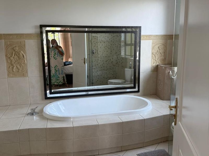 A bathroom featuring a built-in bathtub with tiled surround, decorative wall accents, a large mirror, and a glass-enclosed shower area.