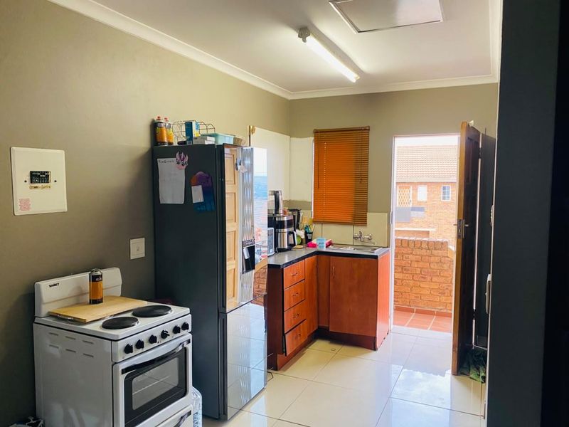 Functional kitchen featuring tiled flooring, wooden cabinetry, electric stove, and direct access to an outdoor balcony area.
