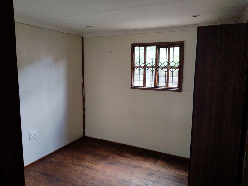 An empty bedroom featuring timber flooring, security burglar bars on the window, and built-in cupboard storage.