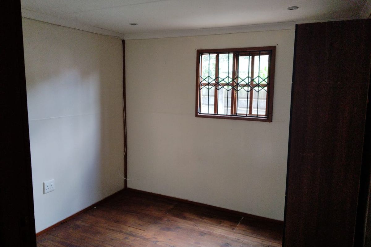An empty bedroom featuring timber flooring, security burglar bars on the window, and built-in cupboard storage.