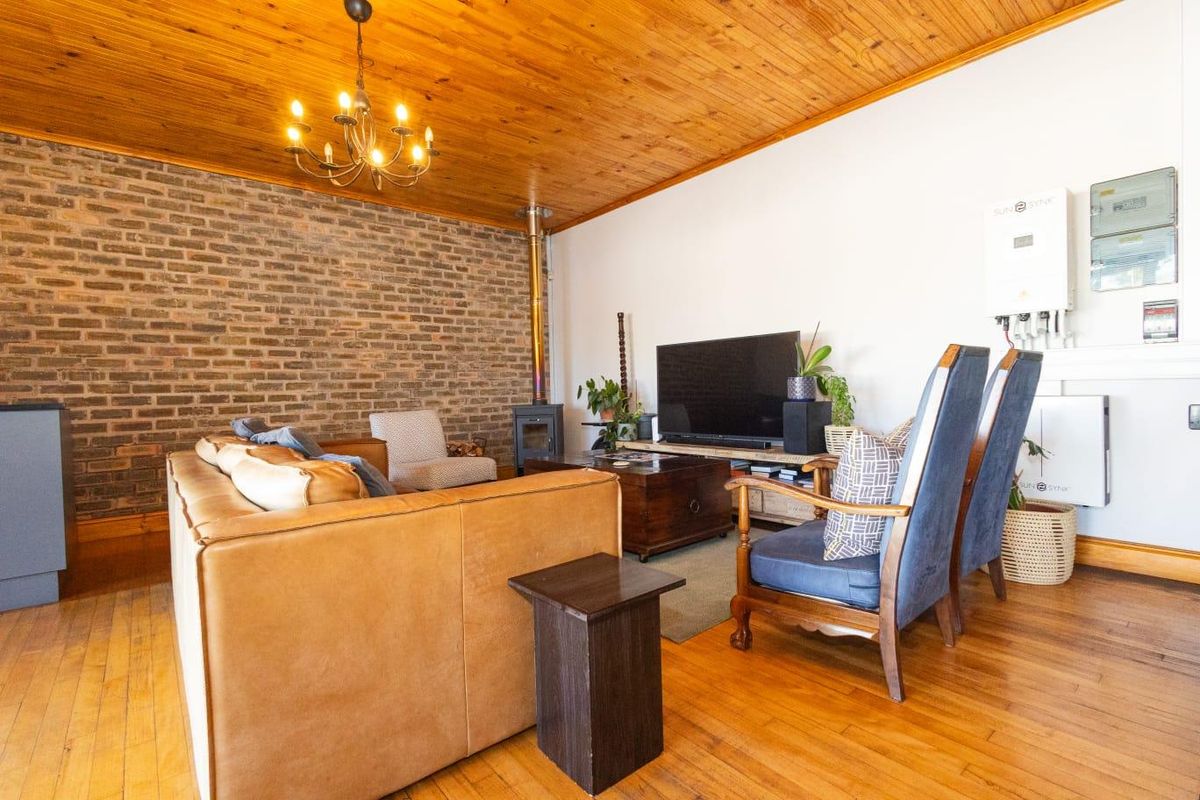 Spacious living room featuring a warm timber ceiling, hardwood flooring, an exposed brick feature wall, and a built-in wood burning fireplace.
