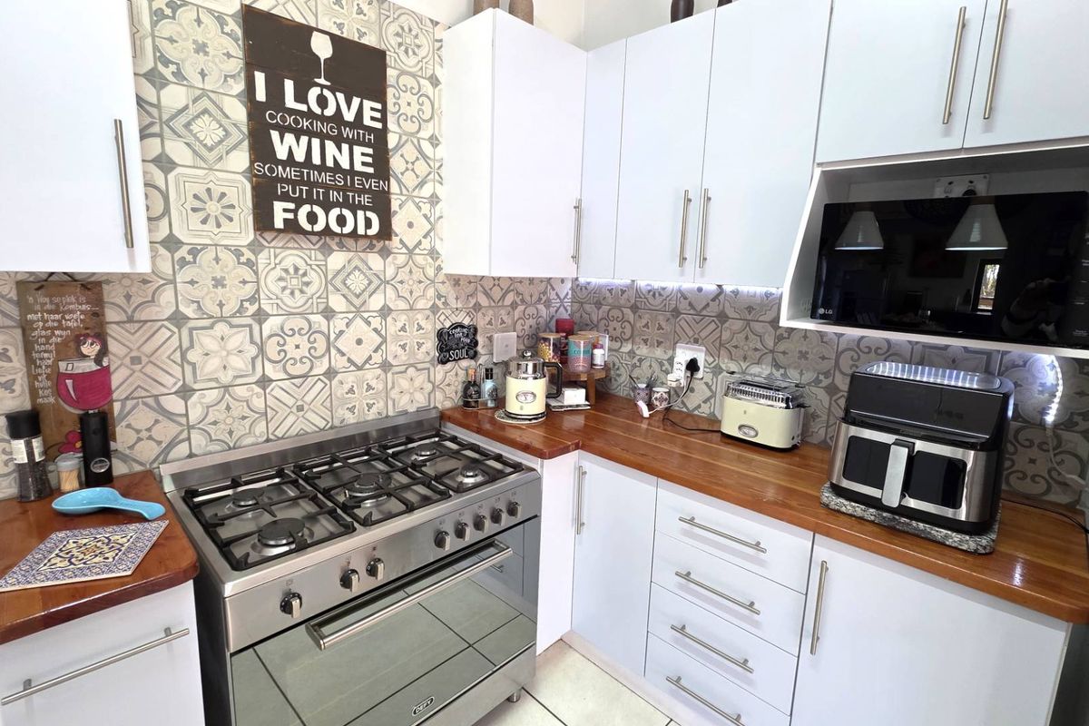 Modern kitchen featuring white cabinetry, warm wooden countertops, a gas stove with oven, and a decorative patterned tile backsplash.