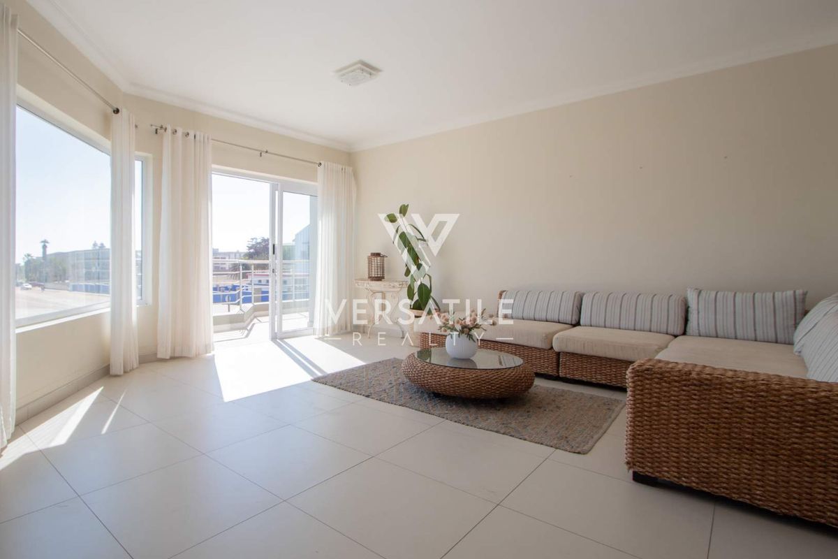 Bright and spacious living area featuring large windows, tiled flooring, and direct access to a balcony through a sliding glass door.