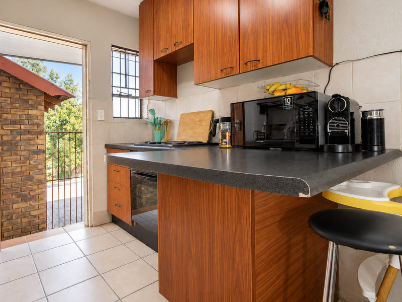 Compact kitchen featuring wood-look cabinetry, laminate countertops, and tiled flooring, with direct access to an outdoor patio area.