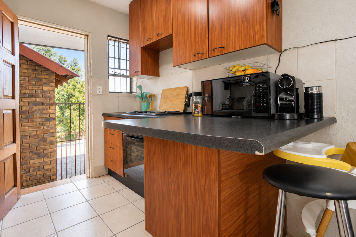Compact kitchen featuring wood-look cabinetry, laminate countertops, and tiled flooring, with direct access to an outdoor patio area.