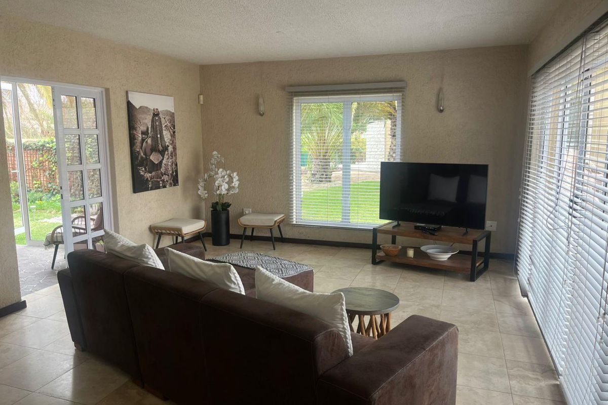 A bright living room featuring tiled flooring, large sliding glass doors providing garden access, and neutral wall finishes with integrated lighting.