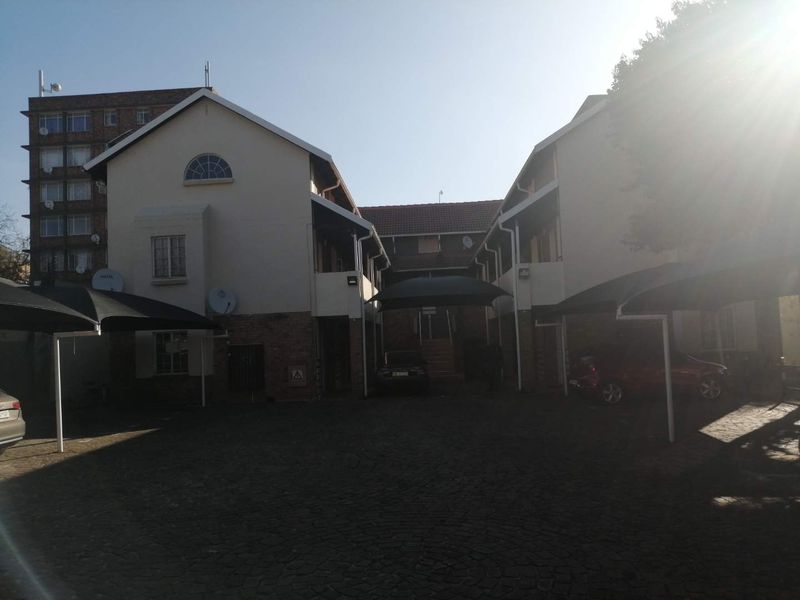 Front exterior view of the apartment complex featuring a paved driveway, covered parking bays, and brick and plaster building facades.