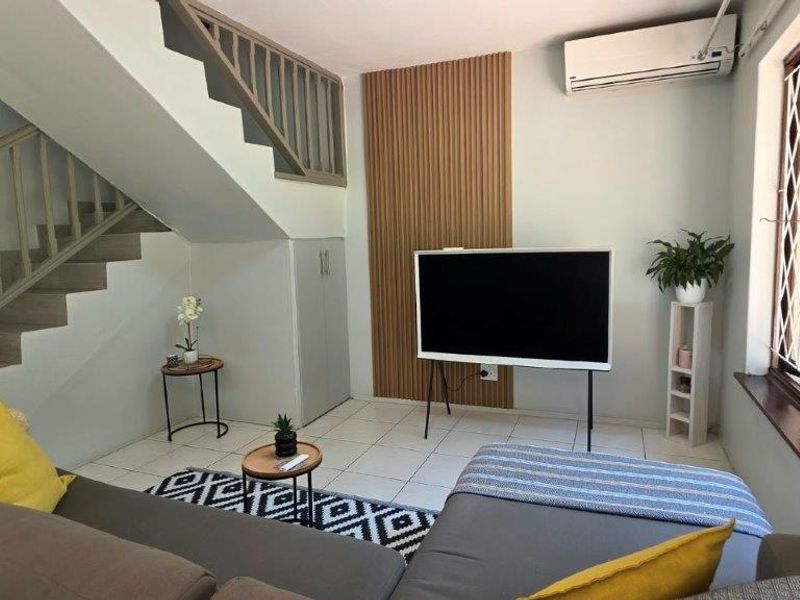 A well-maintained living room featuring a staircase with a wooden balustrade, decorative slatted wall paneling, and a wall-mounted air conditioning unit.