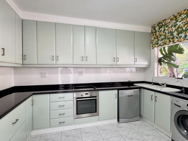 A functional kitchen featuring light-toned cabinetry, black granite countertops, built-in oven and hob, and tiled flooring with space for laundry appliances.