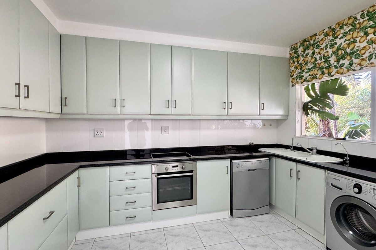 A functional kitchen featuring light-toned cabinetry, black granite countertops, built-in oven and hob, and tiled flooring with space for laundry appliances.