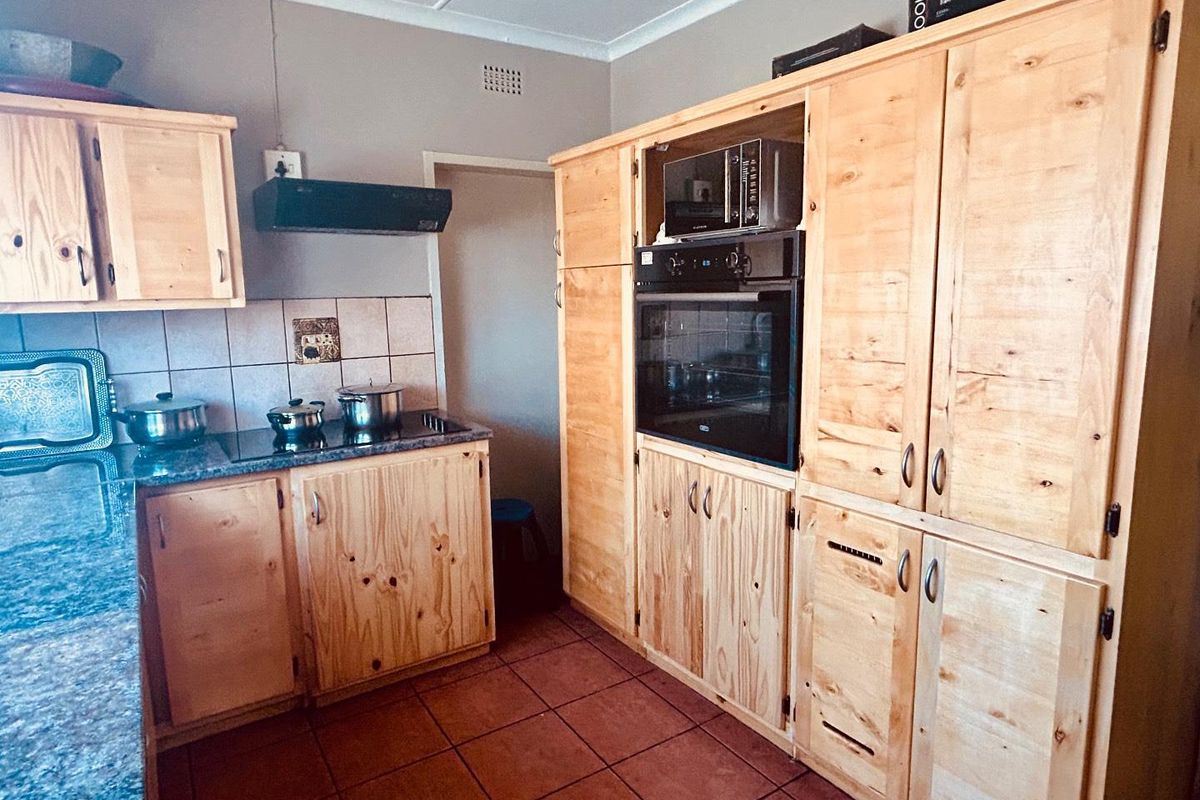A functional kitchen featuring natural wood cabinetry, built-in oven, microwave, and a dark stone-look countertop with tiled splashback.