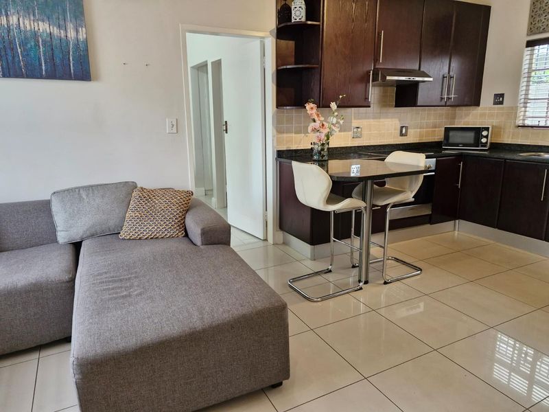 Open-plan living area featuring a kitchen with dark wood cabinetry, granite countertops, and tiled flooring, seamlessly connected to the lounge space.