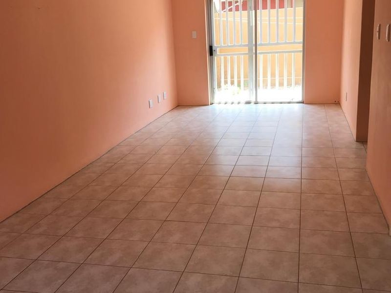 An empty, open-plan living area featuring tiled flooring and a sliding glass door with security gate, leading to an outdoor space.