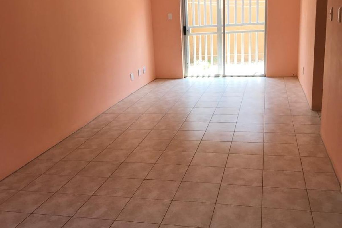 An empty, open-plan living area featuring tiled flooring and a sliding glass door with security gate, leading to an outdoor space.