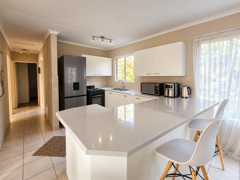 A modern, well-maintained kitchen featuring white cabinetry, quartz countertops, a breakfast bar, and tiled flooring, offering a clean and functional culinary space.