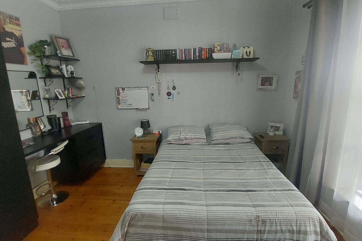 A bedroom featuring polished timber flooring, decorative ceiling cornicing, and a large window with curtain treatments.