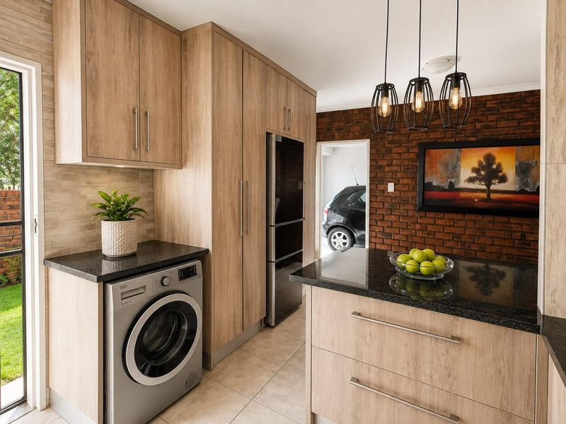 Modern kitchen featuring light wood cabinetry, granite countertops, exposed brick feature wall, and tiled flooring with direct access to the exterior.