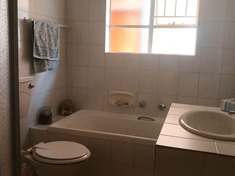 A functional bathroom featuring a built-in bathtub, tiled vanity with a drop-in sink, and a separate shower enclosure with tiled wall finishes.