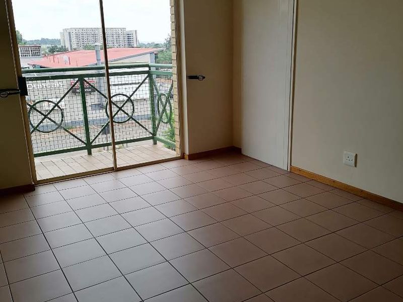 An empty bedroom featuring tiled flooring, a built-in cupboard, and a sliding glass door providing access to a private balcony.