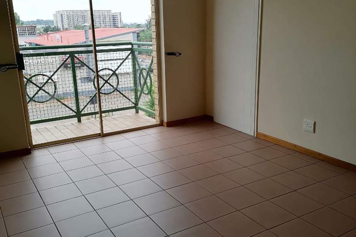 An empty bedroom featuring tiled flooring, a built-in cupboard, and a sliding glass door providing access to a private balcony.