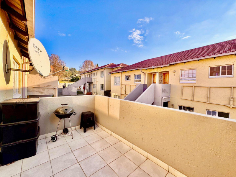 An open-air balcony featuring tiled flooring and a parapet wall, overlooking the apartment complex grounds.