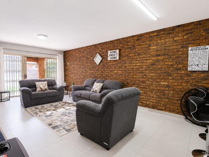 Spacious open-plan living area featuring a striking exposed brick wall, neutral tiled flooring, and direct access to the outdoor patio through sliding glass doors.