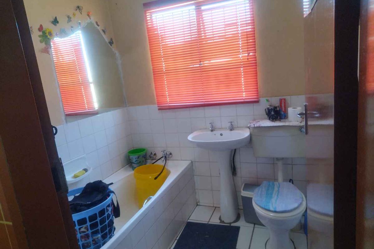 A functional bathroom featuring a standard bathtub, pedestal basin, and toilet with tiled flooring and walls.