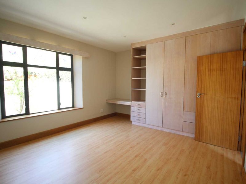 A bright, empty bedroom featuring light wood-look laminate flooring, built-in cupboards with integrated shelving, and a built-in desk area.