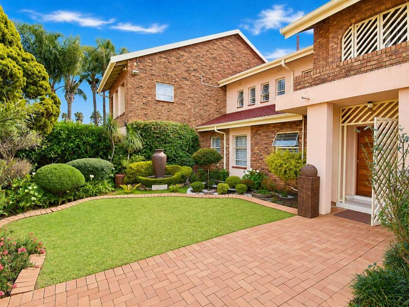 A well-maintained front entrance featuring a brick facade, paved driveway, and a beautifully landscaped garden with a central water feature.