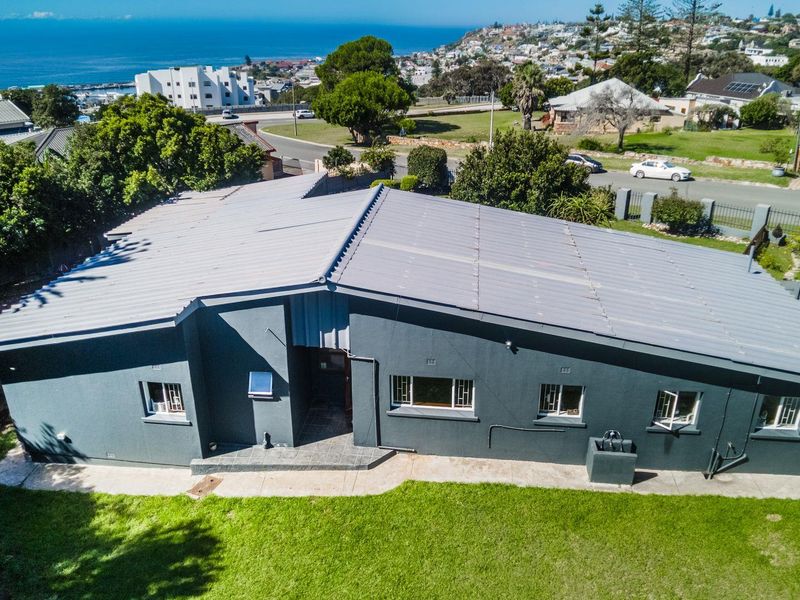 Aerial view of the property showing the metal roof, exterior walls, and surrounding garden area with a coastal neighborhood backdrop.