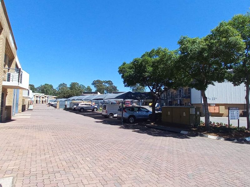 Exterior view of an industrial business park featuring paved driveway access, shade cloth parking bays, and face brick warehouse units.
