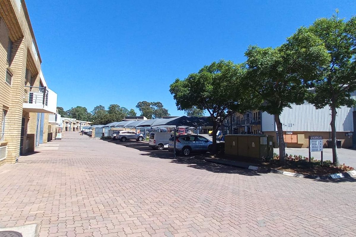 Exterior view of an industrial business park featuring paved driveway access, shade cloth parking bays, and face brick warehouse units.