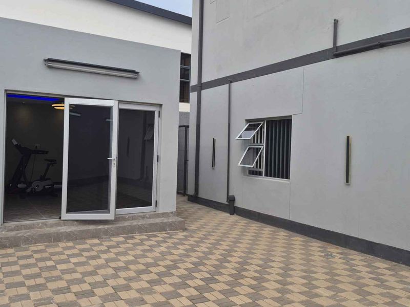 A clean, paved rear courtyard area featuring modern grey exterior walls, sliding glass doors, and functional casement windows.