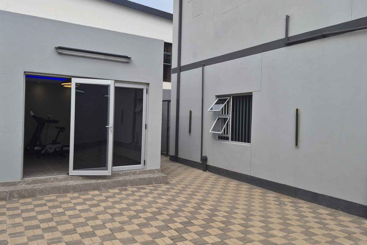 A clean, paved rear courtyard area featuring modern grey exterior walls, sliding glass doors, and functional casement windows.