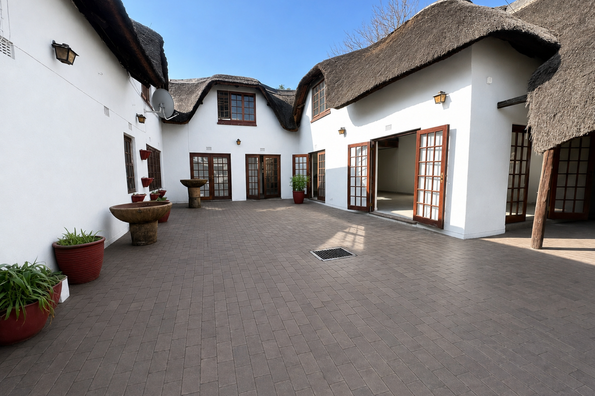 A spacious paved courtyard featuring traditional thatch roofing, multiple sets of wooden french doors, and integrated exterior lighting.