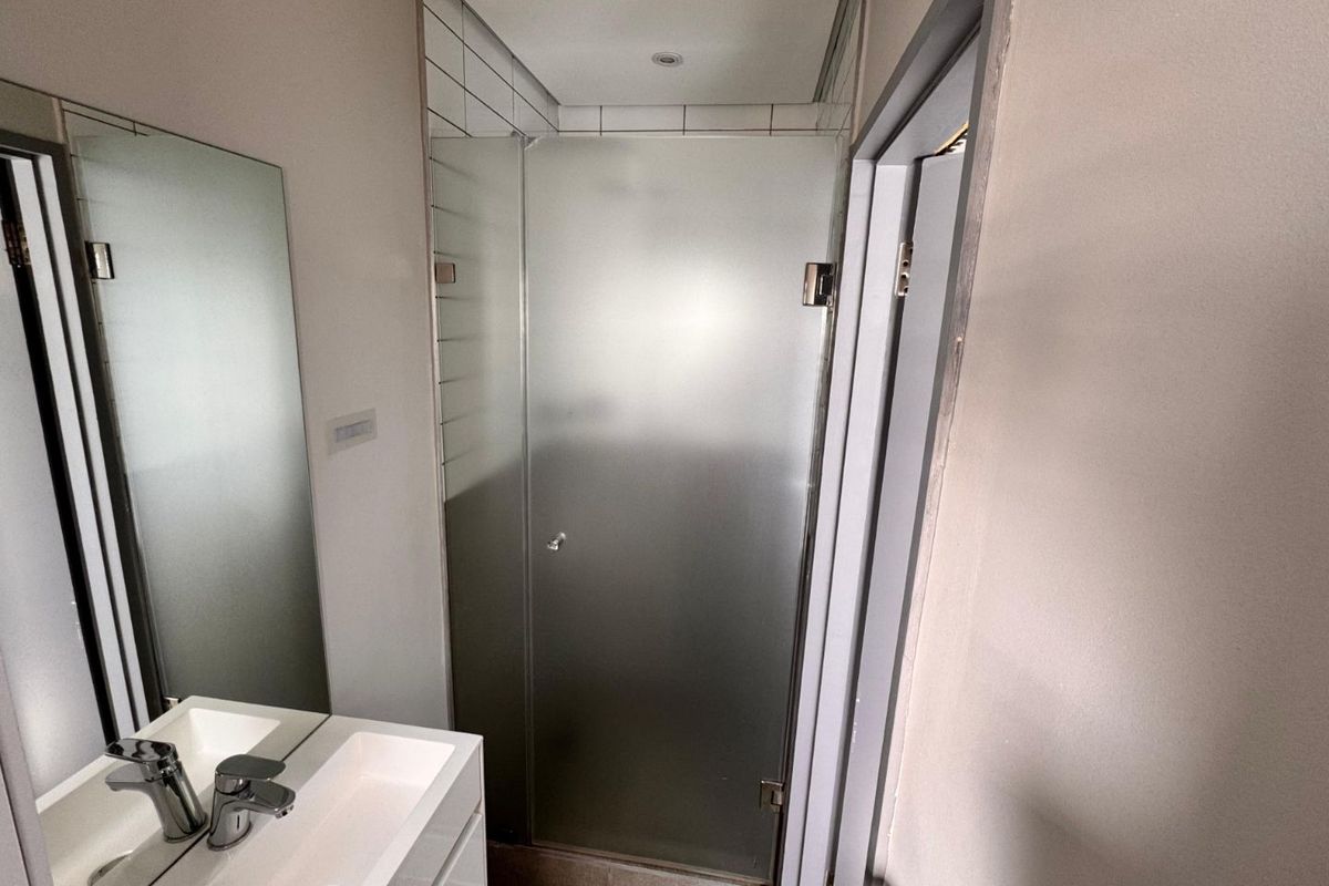 A modern bathroom featuring a vanity basin with a mixer tap, a large wall-mounted mirror, and a tiled shower enclosure with a frosted glass door.