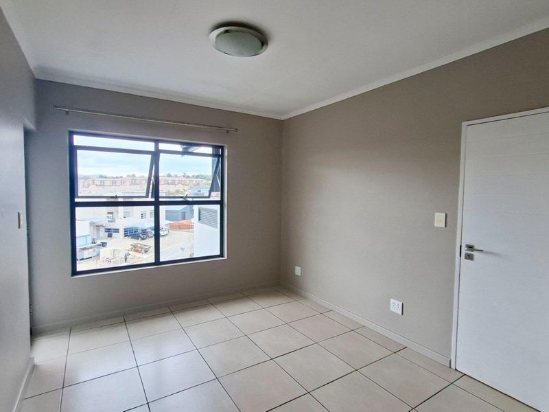 A bright, empty bedroom featuring neutral wall tones, tiled flooring, and a large window providing natural light and an urban view.