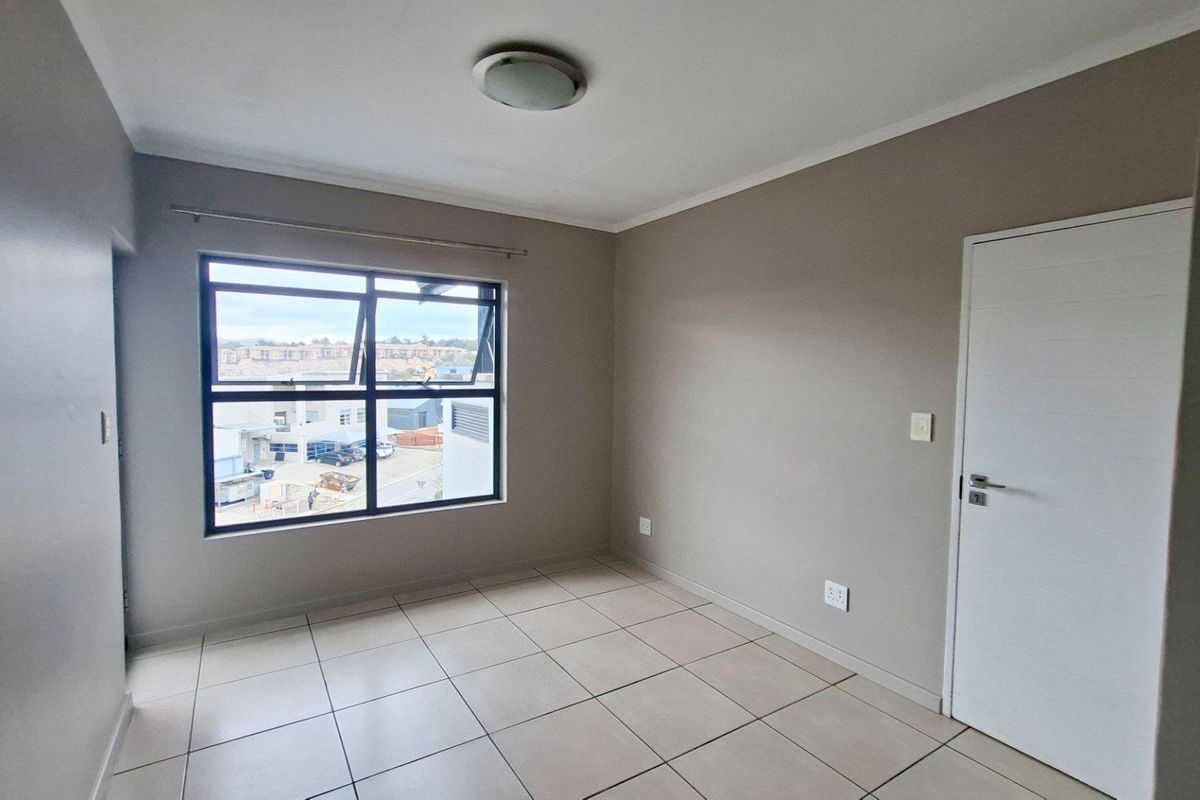 A bright, empty bedroom featuring neutral wall tones, tiled flooring, and a large window providing natural light and an urban view.