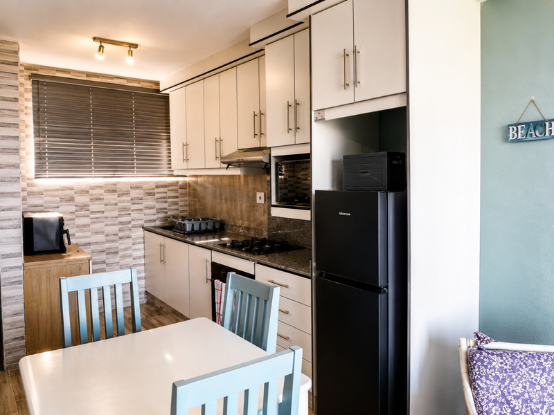 A compact, well-maintained kitchen featuring modern cabinetry, granite countertops, a gas hob, and an integrated oven, complemented by a tiled backsplash and venetian blinds.