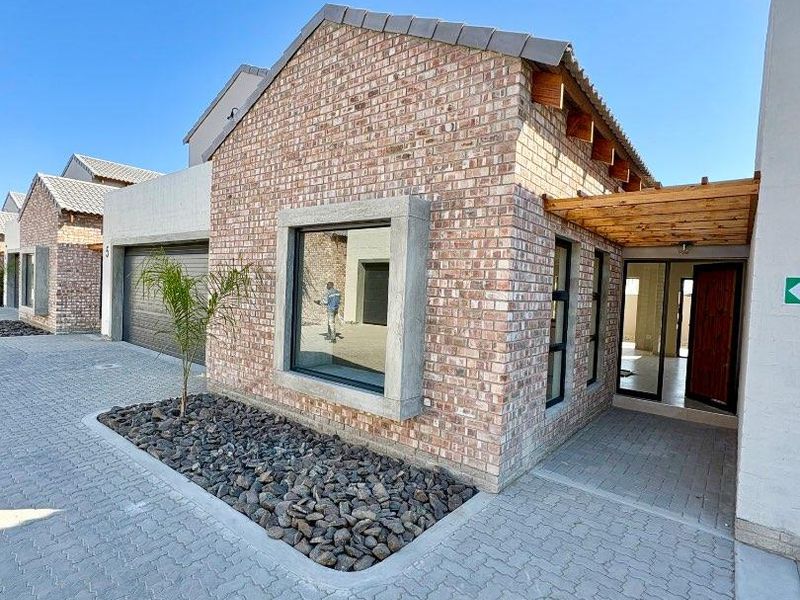 Front elevation of a modern townhouse featuring face-brick construction, a timber pergola entrance, paved driveway, and integrated garage.