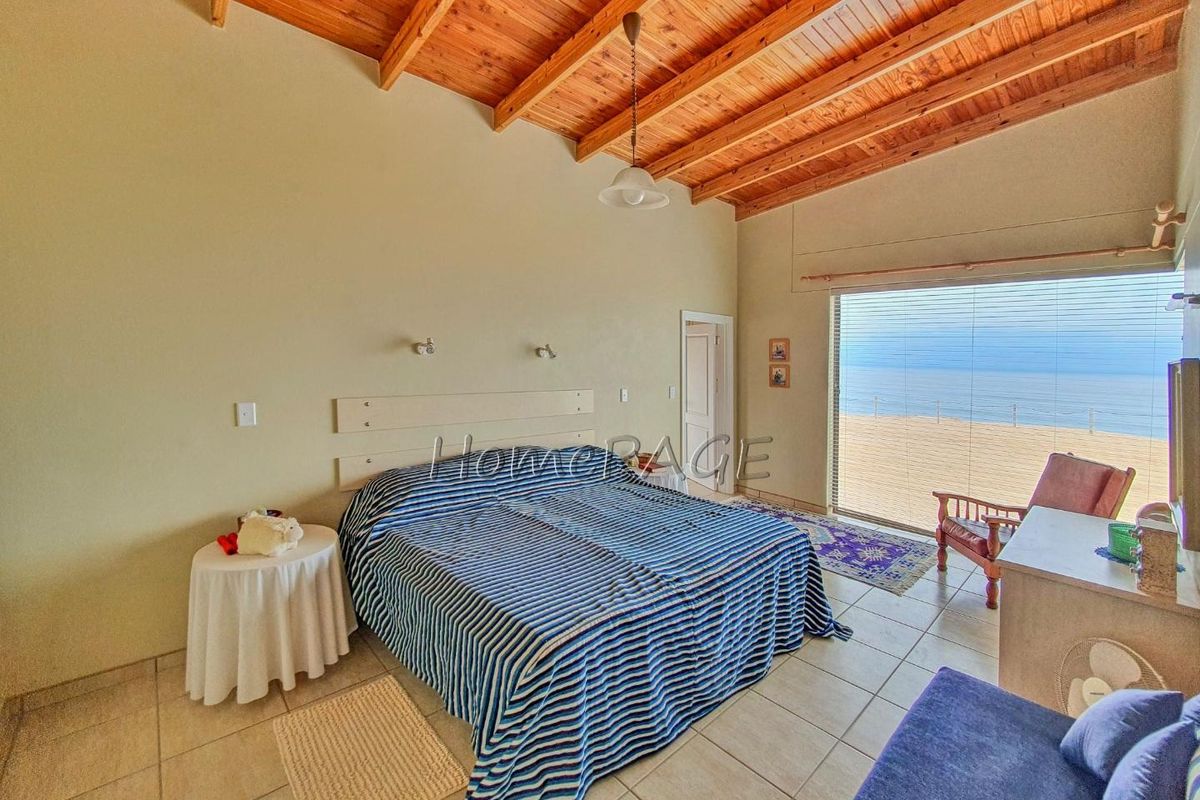 Spacious bedroom featuring a high vaulted timber ceiling, tiled flooring, and large sliding glass doors offering direct ocean views.